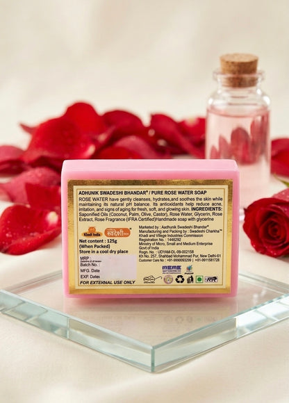 Bar of soap with a label on a glass surface with red rose petals and a bottle in the background.